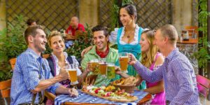 Gäste im Biergarten des Weltenburger am Dom stoßen mit Weltenburger Bier bei einer gemütlichen Brotzeit an