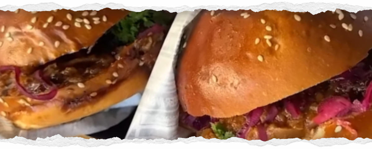 Nahaufnahme zweier Hälften eines veganen Burgers mit Sesambrötchen. Die Burger sind reichlich mit rotem Krautsalat, grünen Blättern und einer dunklen BBQ Soße belegt