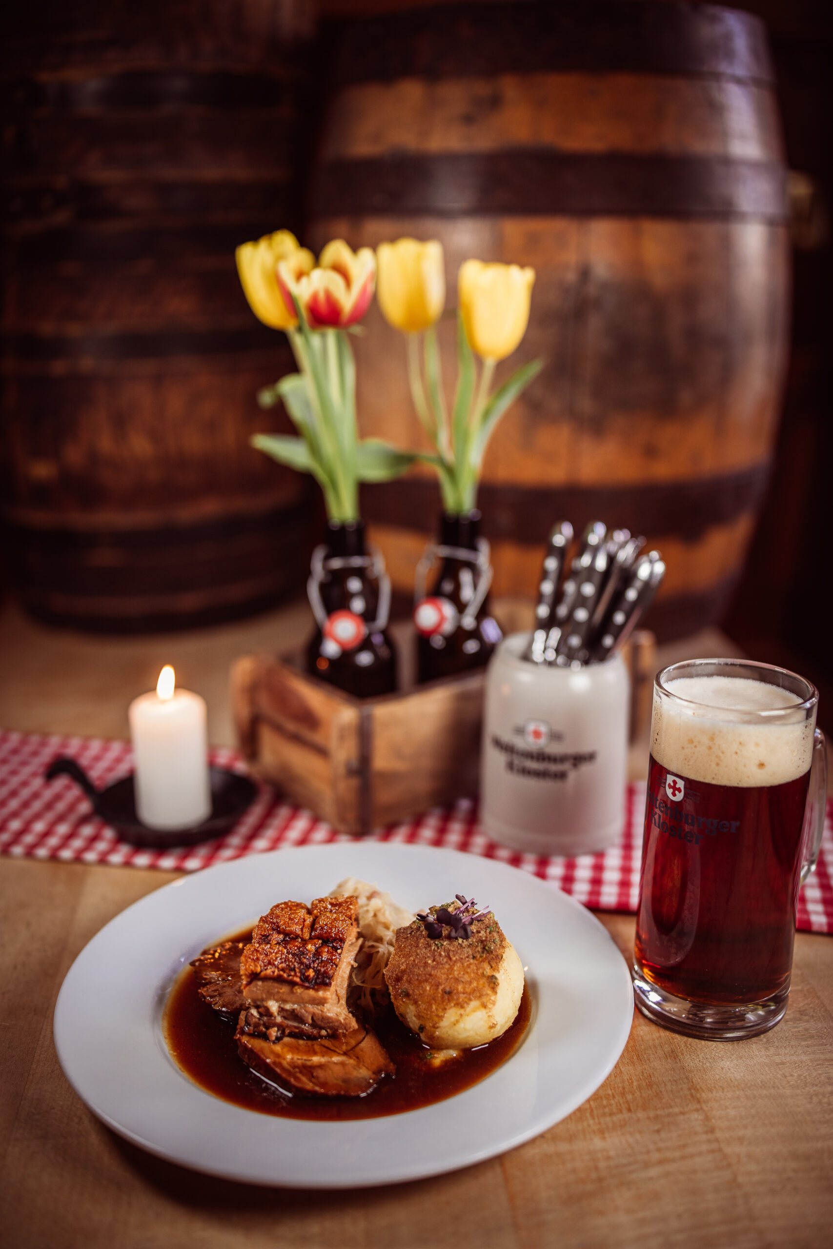 Eine appetitliche Aufnahme eines Schweinebratens angerichtet auf einem traditionell urigen Tisch. Rechts daneben steht ein Weltenburger Klosterbier